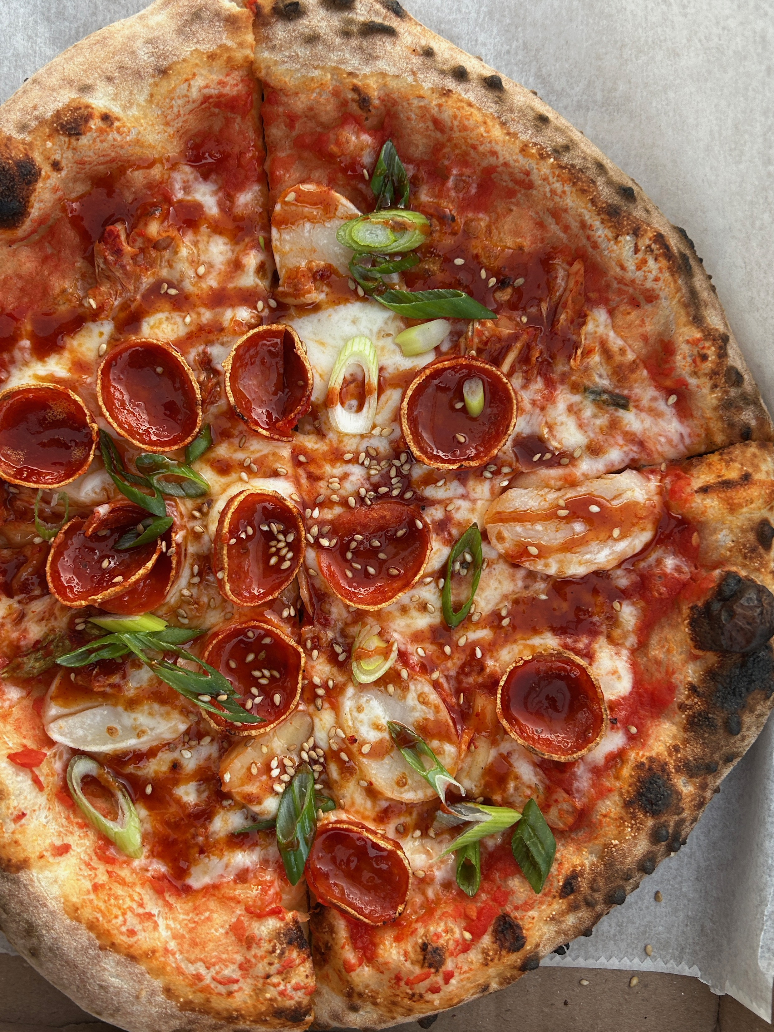 Korean street food-inspired Seoul Street artisanal pizza with red sauce, mozzarella, chewy rice cake, pepperoni, house-made kimchi, gochujang glaze, scallions, and roasted sesame seeds at Pizzeria Coco pizza catering event.